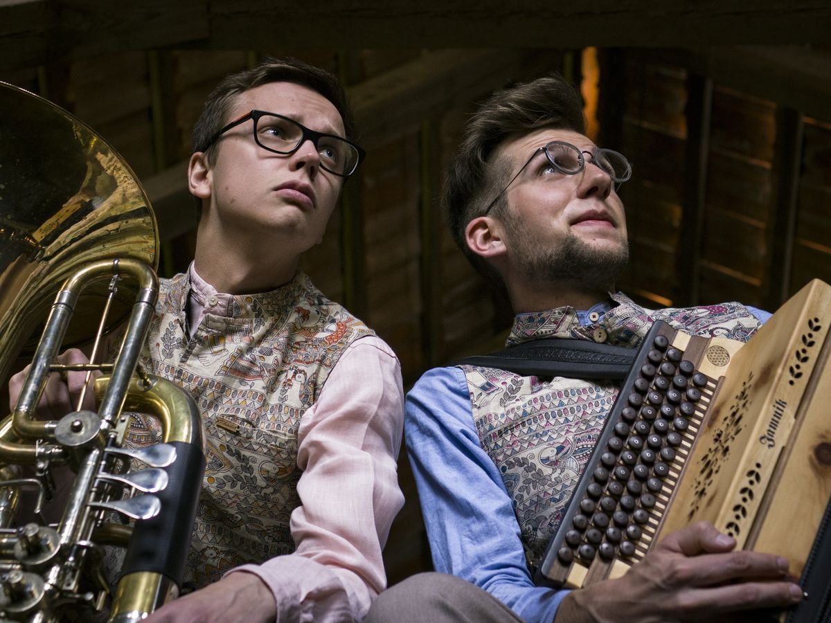 Tobias Weiß mit Tuba und Jonny Kölbl mit Steirischer Harmonika sitzen in einem holzverkleideten Dachboden und blicken nach oben.