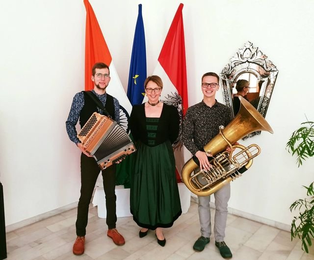 Das Duo mit Harmonika und Tuba vor Fahnen, zusammen mit einer Frau in Tracht.